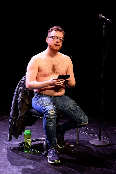 A picture of a topless man sitting in a chair and holding an e-reader.