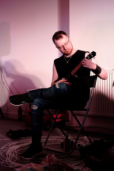 A picture of a man sitting in a chair and playing the ukulele.